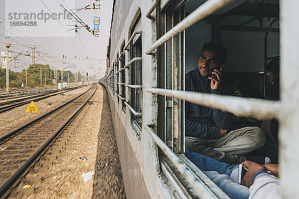 Junger Mann  der auf dem Weg von Neu-Delhi nach Agra in einem Schlafwagenzug mit dem Handy telefoniert.