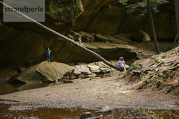 zwei kleine Kinder spielen in einer felsigen Sandsteinschlucht an einem Bach in der Sonne