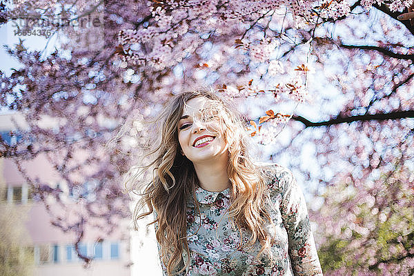 Junge Frau lächelnd vor dem Frühlingsblütenbaum