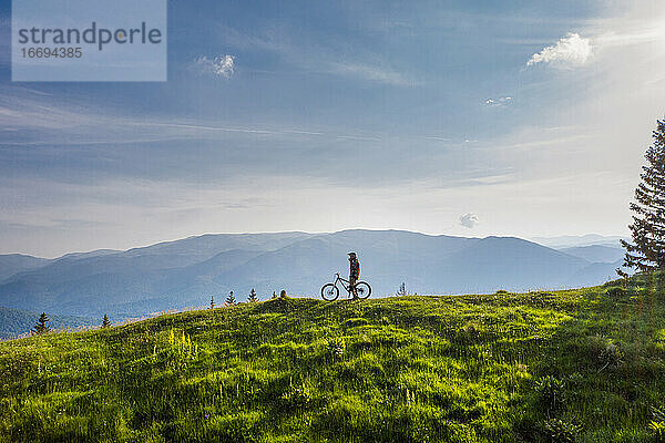 Mountainbiker auf seinem Fahrrad auf einem grünen Hügel an einem sonnigen Tag