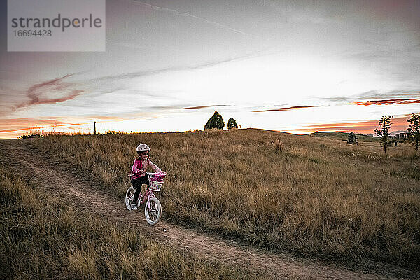 junges Mädchen radelt bei Sonnenuntergang einen grasbewachsenen Hügel hinunter