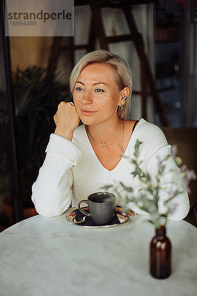 Blonde stilvolle Frau sitzt allein am Tisch mit einer Tasse Kaffee