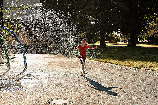 Fröhliches Kind spielt im Wasser in einem Park