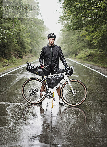 männlicher Fahrradpacker steht mit Fahrrad auf der Straße im strömenden Regen  Maine