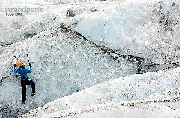 Frau klettert an der Eiswand des Sólheimajökull-Gletschers in Island