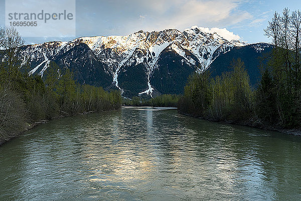 An einem Frühlingstag in den Coast Mountains von British Columbia geht die Sonne über dem noch schneebedeckten Mount Currie unter  während im Vordergrund der Lillooet River fließt.
