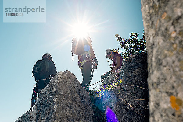 Konzept: Abenteuer. Drei Personen mit Klettergurt  Rucksack. Stehend auf der Spitze des Felsens mit hinterleuchteten Sonne Stern.