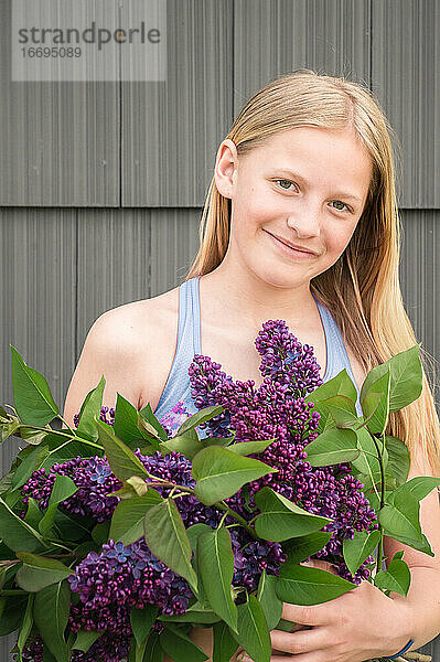 Tween Girl Holding Bunch of Purple Lilac Blumen und lächelnd