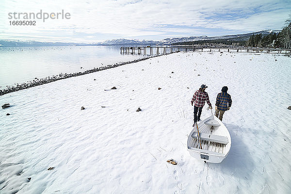 Zwei Männer ziehen ein weißes Ruderboot über ein verschneites Ufer in South Lake Tahoe  CA