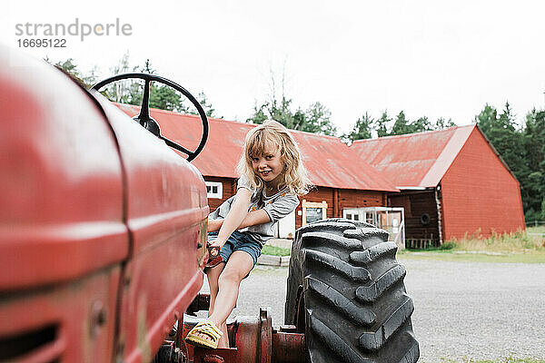 Mädchen sitzt auf einem Traktor und lächelt  während sie auf einem Bauernhof in Schweden ist