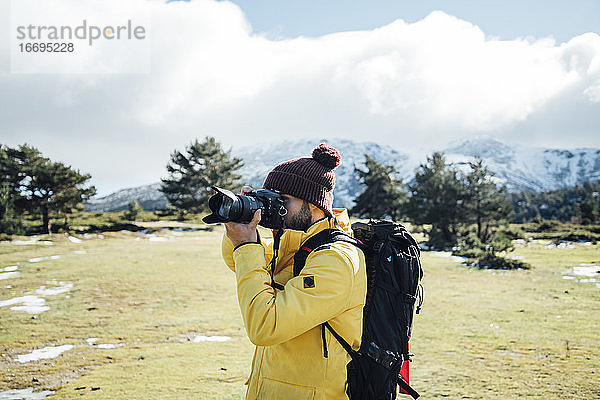Junger Mann mit gelber Jacke und Rucksack beim Fotografieren auf dem Berg