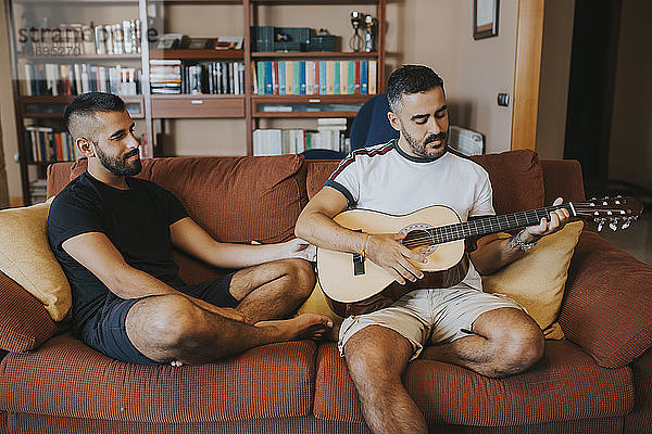 Junge spielt Gitarre auf der Couch sitzend sein Freund