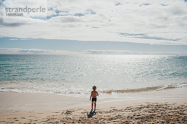 Junge  der an einem sonnigen Tag im Urlaub am Strand ins Wasser geht