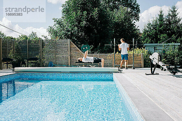 zwei Männer trainieren zusammen am Pool im heimischen Fitnessstudio