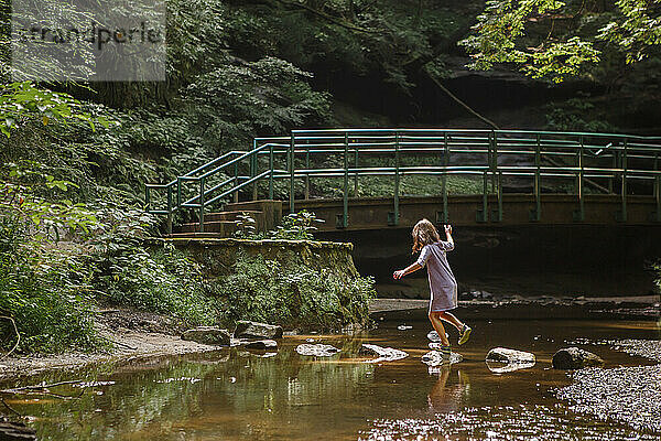 Ein kleines Mädchen balanciert auf Trittsteinen über einen Bach im Wald