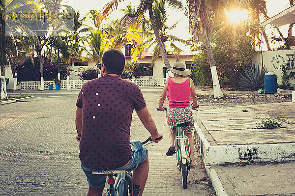 Mann und Frau auf Fahrrädern bei Sonnenuntergang mit Palmen