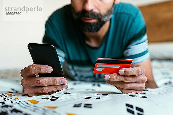 Close up Hand hält Kreditkarte und Online-Shopping auf dem Bett.
