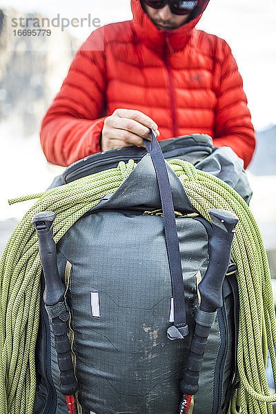 Detailaufnahme eines Rucksacktouristen  der ein Seil an seinem Rucksack befestigt.