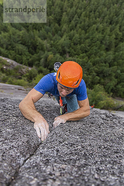 Kletterer  der beim Klettern nach oben blickt und sich auf den nächsten schwierigen Schritt konzentriert