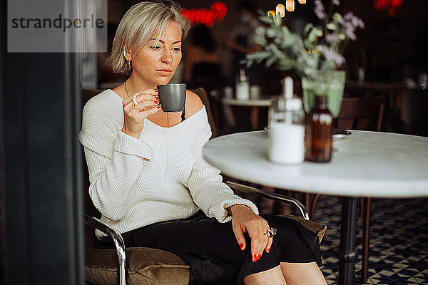 Frau trinkt Kaffee und schaut traurig  während sie allein am Tisch im Café sitzt