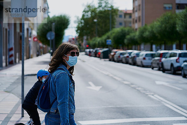 Frau auf der anderen Straßenseite mit einer Maske und Sonnenbrille