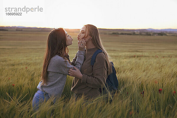 zwei Frauen halten sich bei Sonnenuntergang auf einem Feld an den Händen