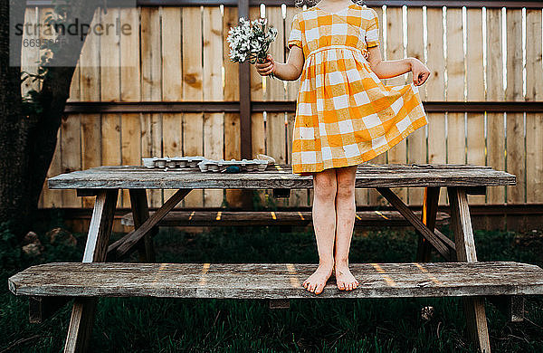 Junges Mädchen mit gelbem Kleid und Blumen auf einem Stehtisch