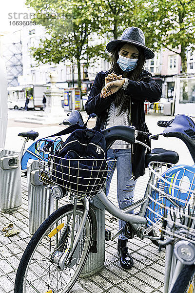 Junge Frau mit Maske wählt ein Fahrrad an einer öffentlichen Verleihstelle