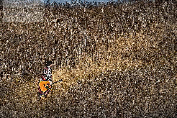 Country-Musiker mit Akustikgitarre geht in Gräsern auf einem Feld