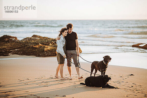 Weitwinkelansicht eines Millennial-Paares  das mit Hunden am Ufer steht