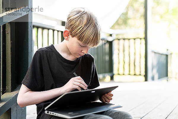 Tween sitzt draußen auf der Veranda und benutzt ein Touchscreen-Tablet mit Stift