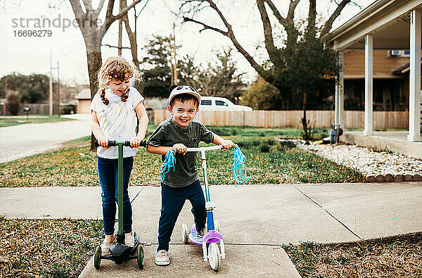 Junge Brüder und Schwestern fahren Roller im Vorgarten