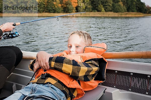 Junge sitzt entspannt auf einem Boot  während er angelt