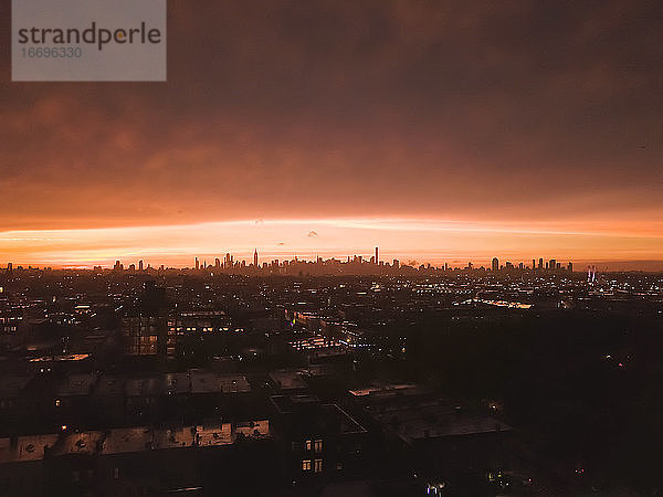 Luftaufnahme von Brooklyn über weit weg Manhattan Skyline in der Ferne nach Sonnenuntergang mit feuerrotem Licht und Wolkenkratzer Silhouette