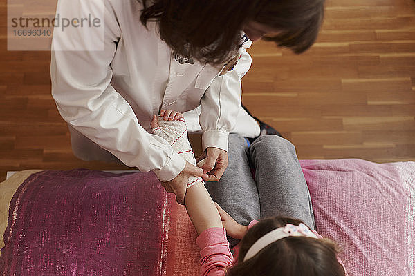 Draufsicht auf eine Ärztin  die den Arm eines kleinen Mädchens in ihrem Zimmer verbindet. Hausarzt Konzept