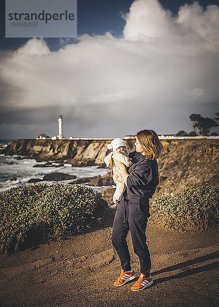 Eine Frau hält ein Baby in der Nähe eines Leuchtturms an der Pazifikküste