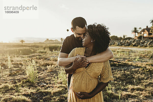 Junges Ehepaar umarmt die Schwangerschaft am Strand
