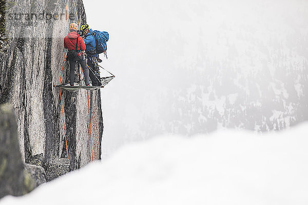 Zwei Bergsteiger stehen auf dem Portaledge und schlagen ihr Nachtlager auf.