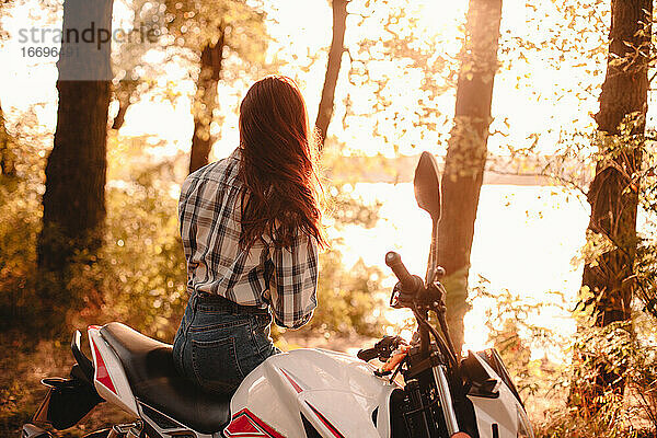 Junge Frau  die auf einem Motorrad sitzend die Aussicht betrachtet und sich am Fluss entspannt