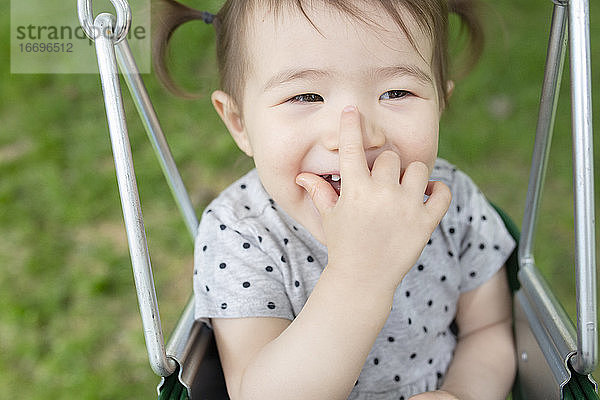 Adorable Baby Girl lächelt mit der Hand über dem Mund beim Schwingen im Freien