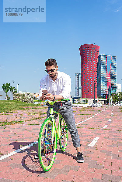 Outdoor-Porträt eines gut aussehenden jungen Mannes mit Mobiltelefon und Fahrrad mit festem Gang auf der Straße.