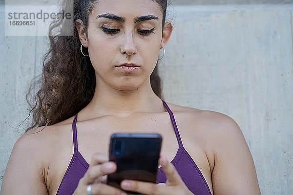 Porträtansicht einer Frau in Sportkleidung  die auf ein Smartphone schaut