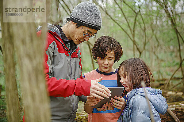 Ein Vater und seine Kinder betrachten bei einem Waldspaziergang im Frühling eine Tafel