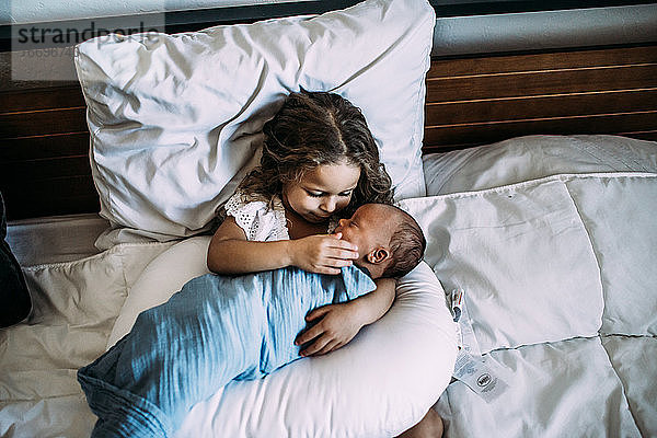 Junges Mädchen hält neugeborenen kleinen Bruder auf dem Bett