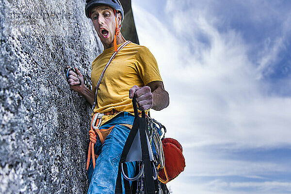 Kletterer hält Portaledge an Wand mit lustigem Gesicht und offenem Mund