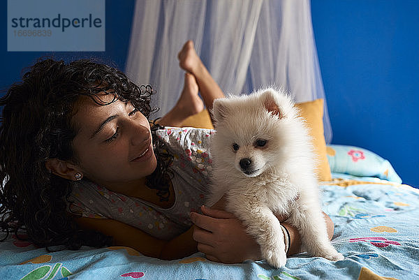 Ein kleines Mädchen schaut auf ihren weißen Pomeranian-Welpen