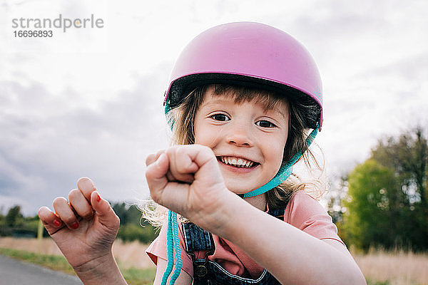 fröhliches Porträt eines jungen Mädchens mit Helm  das draußen spielt