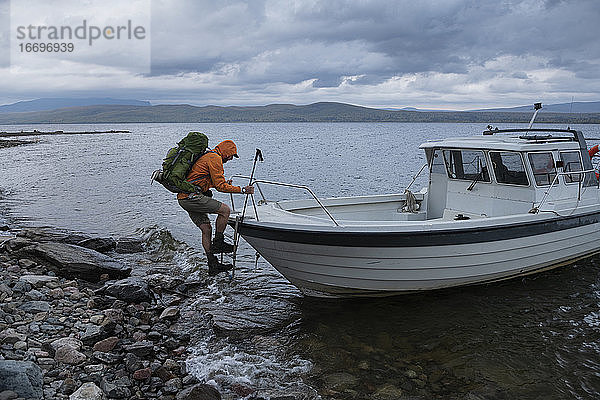 Wanderer klettert über eine kleine Bootsfähre über den See Riebnes auf dem Kungsleden Trail  Lappland  Schweden