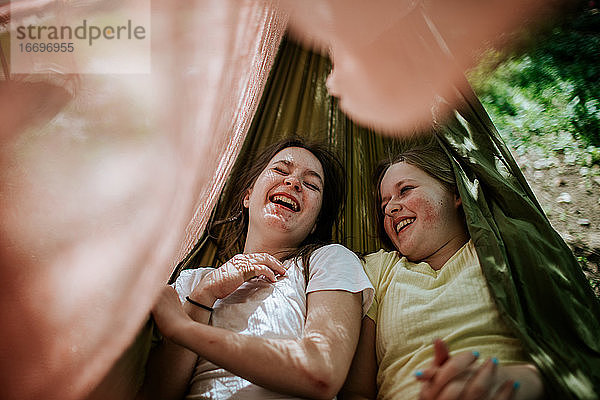 Zwei Teenager-Mädchen liegen in der Hängematte lachend und lächelnd draußen