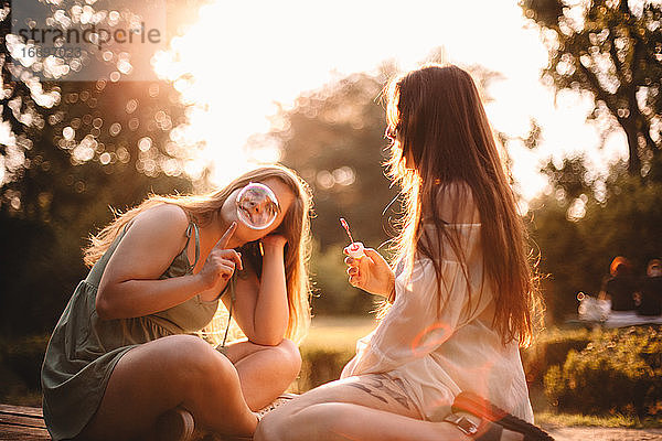 Glückliche Freundinnen spielen mit Seifenblasen im Park im Sommer